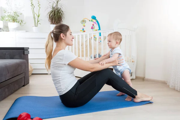 Schattige babyjongen trainen met de jonge moeder op fitness mat thuis — Stockfoto