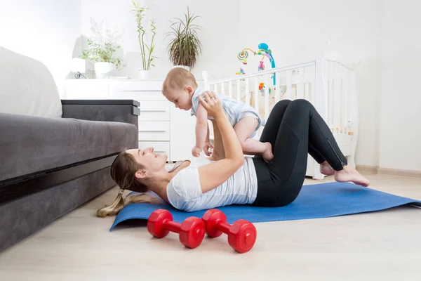 Mujer joven feliz haciendo ejercicio con su bebé en el suelo en la sala de estar — Foto de Stock