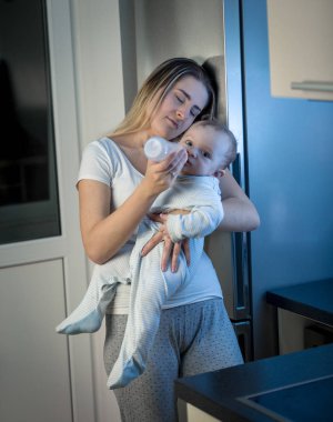 Onun erkek bebek süt ile geceleri biberon uykulu genç anne portresi