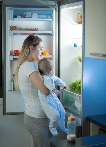 Portrét mladé matky drží její chlapeček a hledají něco k jídlu v lednici v noci — Stock fotografie