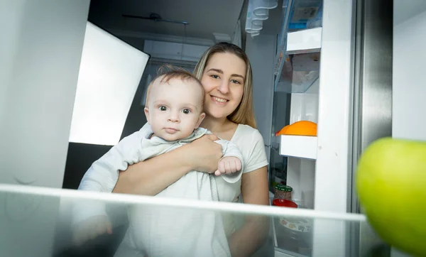 Portrét ospalý maminka s bbay klukem hledá uvnitř chladničky v noci — Stock fotografie