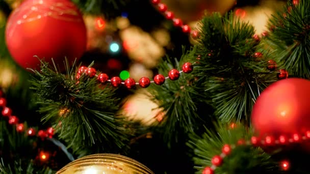 Closeup 4k footage of red and golden baubles hanging on Christmas tree with glowing colorful lights — Stock Video