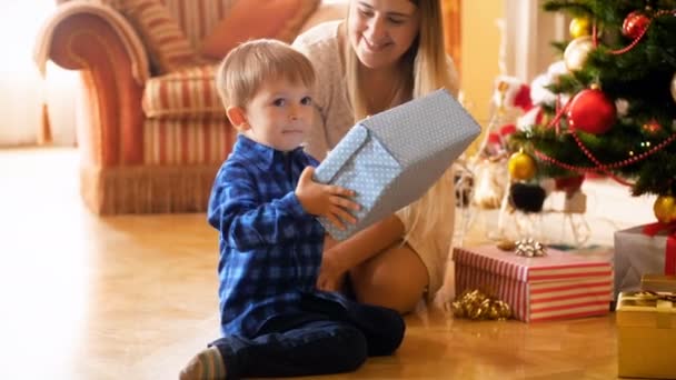 4 k Zdjęcia ładny 3 lata oldd toddler chłopiec otwiera Boże Narodzenie pudełeczka z matka rano — Wideo stockowe