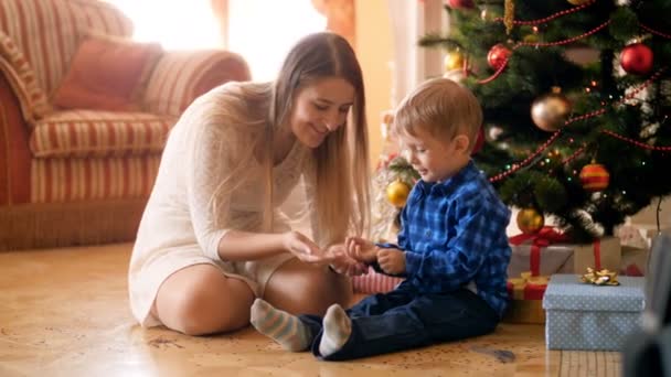 4 k beelden van mooie jonge moeder speelt met haar kleine jongen onder kerstboom en gooien van confetti — Stockvideo