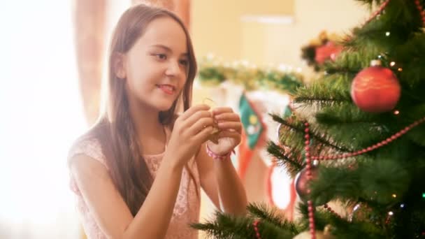 4k vídeo de bela morena adolescente pendurado bugigangas coloridas na árvore de Natal na sala de estar — Vídeo de Stock