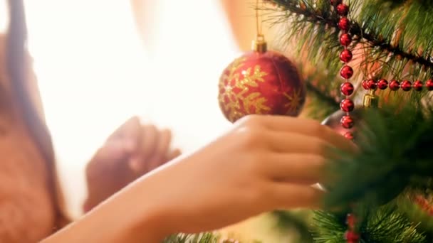 Closeup 4k imagens de meninas mãos colocando bugigangas e contas coloridas na árvore de Natal na manhã — Vídeo de Stock