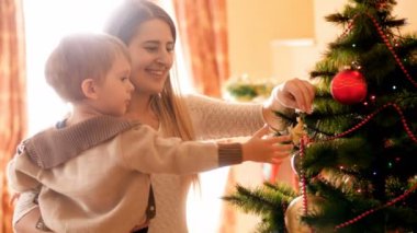 Genç Anne küçük oğlu boncuk ve baubles ile Noel ağacı süsleme öğretim portresi