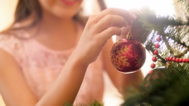 Primer plano 4k metraje de hermosa chica sonriente poniendo rojo brillante bauble en el árbol de Navidad — Vídeos de Stock