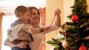 şirin yürümeye başlayan çocuk annesi ile renkli çelenk ve boncuk dekorasyon Noel ağacı ile 4 k görüntüleri