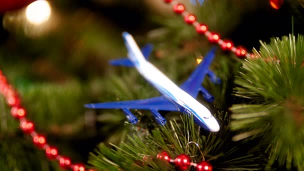 Closeup 4k vídeo de avião em miniatura deitado na árvore de Natal com luzes coloridas brilhantes. Conceito de viajar em férias de inverno — Vídeo de Stock