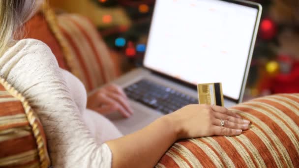 Imágenes de 4k de una mujer sentada en un sillón junto a un brillante árbol de Navidad y buscando regalos de Navidad en Internet — Vídeos de Stock