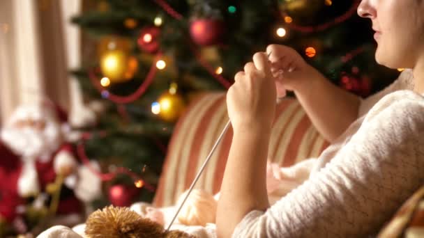 4k video of woman resting in armchair by the glowing Christmas tree and knitting woolen scarf — Stock Video