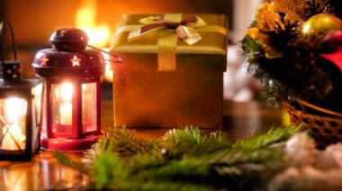 Altın Noel hediye kutusu, mumlar ve yanan şömine karşı ahşap masa üzerinde geleneksel çelenk closeup 4k görüntüleri