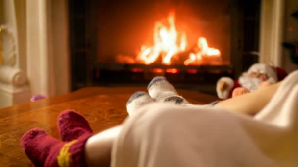 Closeup 4k footage of family feet lying on sofa under blanket warming at burning fireplace — Stock Video