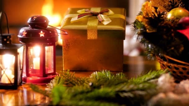 Altın Noel hediye kutusu, mumlar ve yanan şömine karşı ahşap masa üzerinde geleneksel çelenk closeup 4k görüntüleri — Stok video