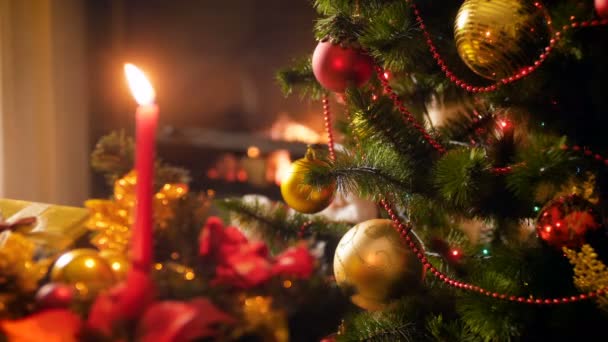 Closeup vídeo 4k de luzes brilhantes na árvore de Natal decorada, vela e lareira em chamas. Fundo perfeito para celebrações e feriados de inverno — Vídeo de Stock