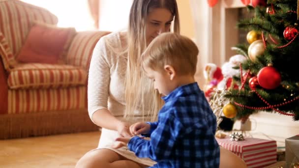 Повільні кадри руху чарівного маленького хлопчика і матері, що грає з конфетті під ялинкою — стокове відео