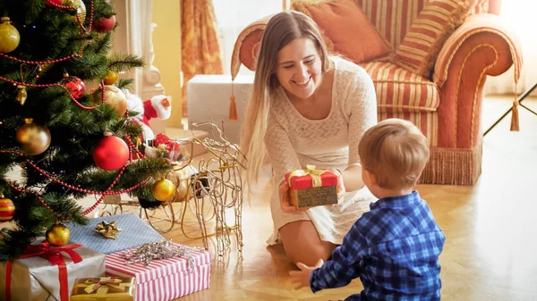 Счастливая улыбающаяся мать дарит рождественский подарок своему маленькому сыну — стоковое фото