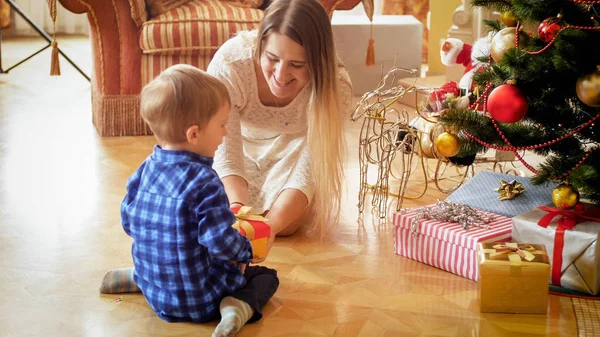 Симпатичный мальчик сидит на полу с матерью и получает рождественский подарок — стоковое фото