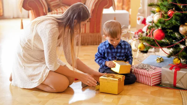 Hermosa joven mujer dando regalos de Navidad a su pequeño niño en la mañana de Navidad — Foto de Stock