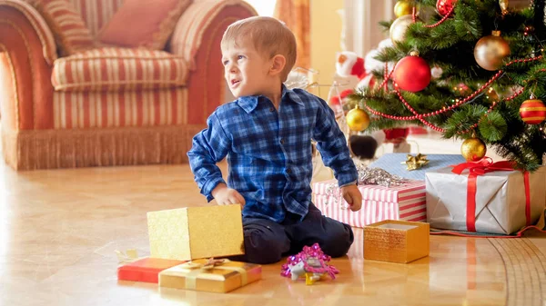 Aufgebrachter kleiner Junge sitzt auf dem Boden und hält Weihnachtsgeschenk in der Hand — Stockfoto