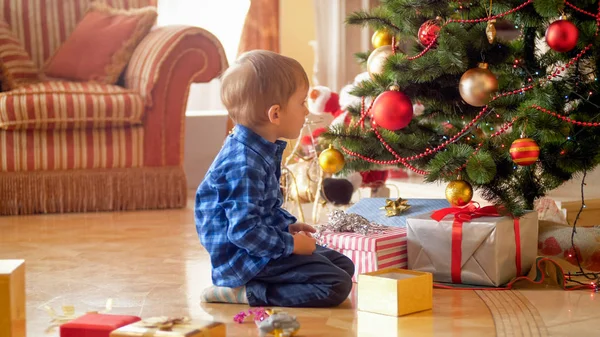 Lindo niño sentado bajo el árbol de Navidad por la mañana — Foto de Stock