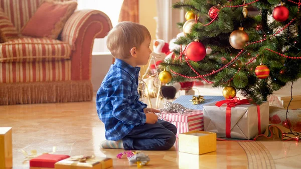 3 anos de idade criança menino sentado no chão e olhando para a árvore de Natal na manhã — Fotografia de Stock