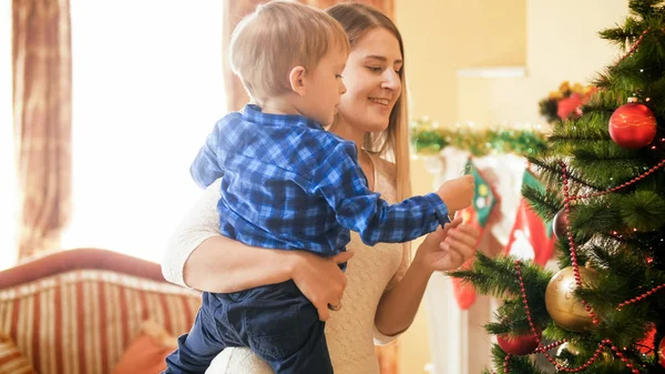 Porträtt av leende ung mor med småbarn son dekorera julgran — Stockfoto