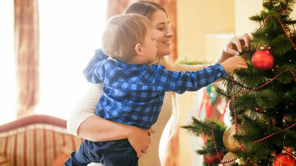 Tonas porträtt av leende ung kvinna med hennes barn son hängande grannlåt på julgran — Stockfoto