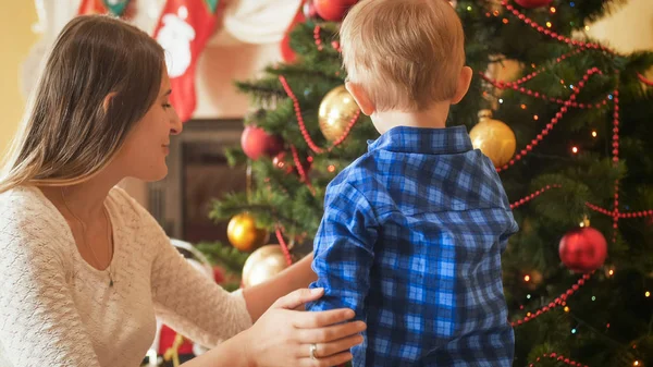 Tonad bild av liten pojke står med mor bredvid julgran i vardagsrummet — Stockfoto