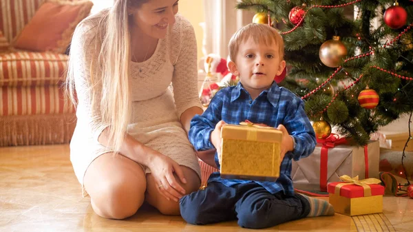 Retrato de niño adorable sosteniendo el regalo de Navidad que recibió de la madre por la mañana — Foto de Stock