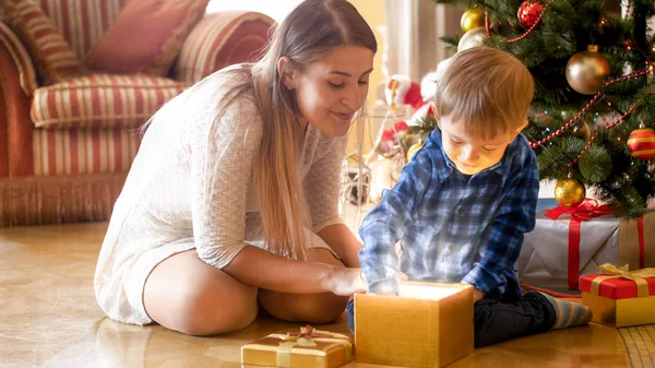 Веселый возбужденный мальчик берет рождественский подарок из светящейся волшебной подарочной коробки — стоковое фото