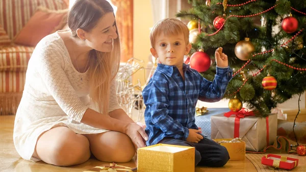 Lyckligt leende mor tittar på sin lilla pojke håller julklapp — Stockfoto