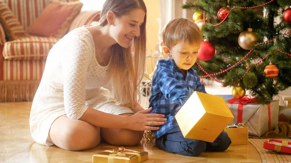 Retrato de menino animado com a mãe levando presente de Natal fora da caixa de presente de ouro — Fotografia de Stock