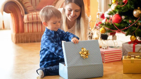 Glad liten pojke öppna julklapp på morgonen under julgranen — Stockfoto