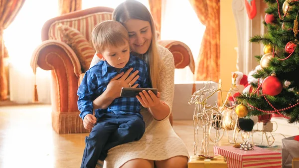 Πορτρέτο του wathcing αγόρι toddler βίντεο στο κινητό τηλέφωνο με τη μητέρα του στο σαλόνι διακοσμημένο για τα Χριστούγεννα — Φωτογραφία Αρχείου