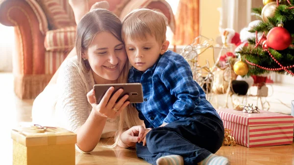 Porträtt av glada mor med småbarn pojken njuter av julen morgon och med smartphone — Stockfoto