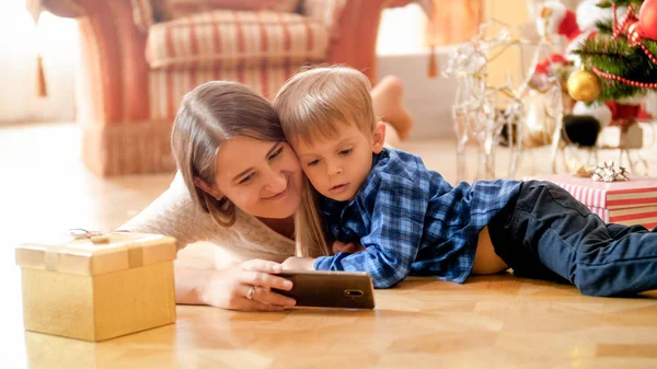 Little toddler boy with mother watching cartoons on phone on Christmas morning — Stock Photo, Image