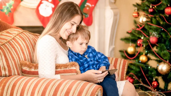 Feliz mãe sorridente com seu filho assistindo vídeo no smartphone no Natal — Fotografia de Stock