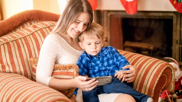 Sorrindo jovem mãe com seu filho assistindo desenhos animados sentados em poltrona na sala de estar — Fotografia de Stock