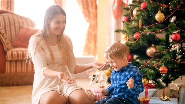 Riendo niño feliz con la madre lanzando confeti colorido en la mañana de Navidad —  Fotos de Stock