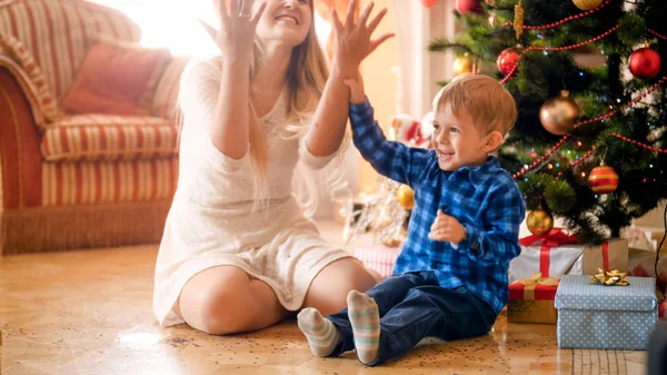 Портрет счастливого смеющегося мальчика, бросающего красочные конфетти с мамой в рождественское утро — стоковое фото