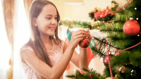 Foto de primer plano de la joven niña msiling decorando el árbol de Navidad con bolas rojas —  Fotos de Stock