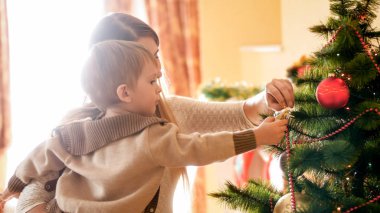 Küçük oğlu tutarak ve ona Noel ağacı süsleme yardım genç kadın portresi