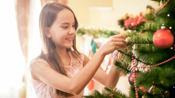 Retrato de menina adolescente sorridente feliz colocando bugigangas coloridas e contas na árvore de Natal — Fotografia de Stock