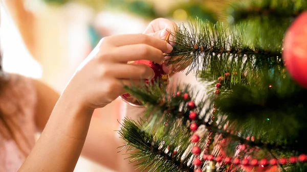 Imagen de cerca de las manos de las niñas poniendo bolas rojas en el árbol de Navidad — Foto de Stock