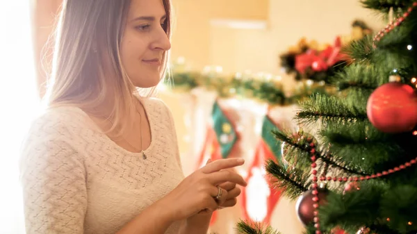 Retrato de close-up de sorrir jovem mulher satnding na sala de estar e olhando na árvore de Natal — Fotografia de Stock