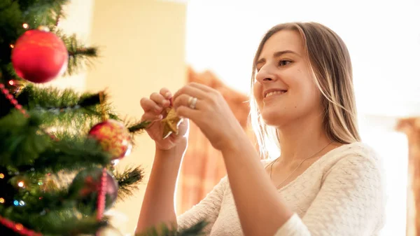 Retrato de una joven sonriente poniendo una estrella dorada decorativa en la rama del árbol de Navidad — Foto de Stock