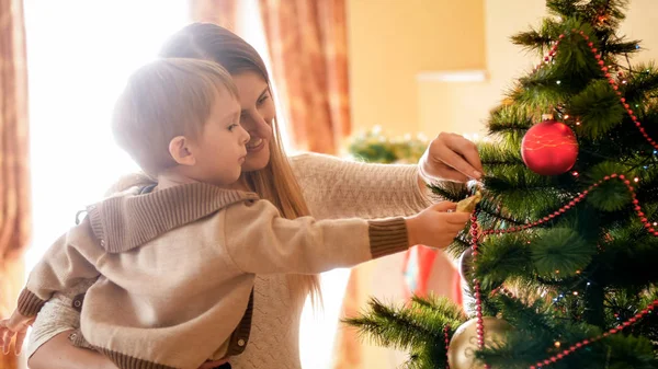 Retrato de feliz madre sonriente con su hijo decroating árbol de Navidad por la mañana — Foto de Stock