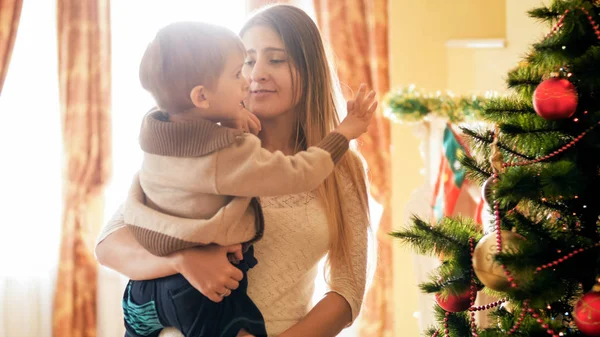 Ung mamma hålla sin lilla pojke att nå för julgranskulor — Stockfoto